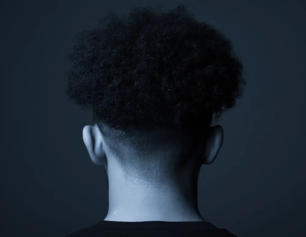 Macro photograph of the back of a head with grown-out coily hair and a soft, unshaped nape line