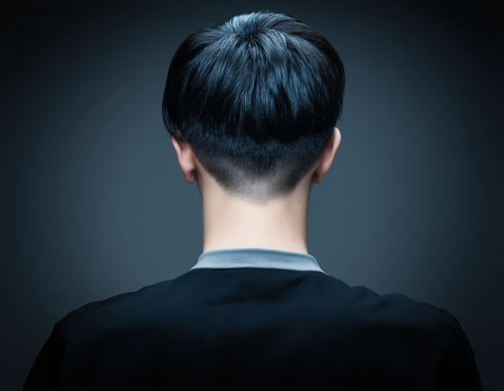 Photograph of a low taper fade in straight dark hair, with a soft graduated blend into a rounded natural neckline