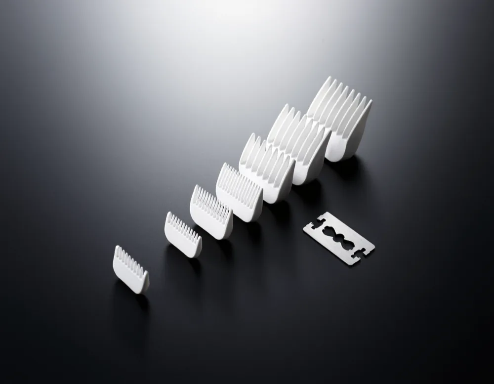 Eight plain clipper guard combs laid out in ascending order on a matte black surface next to a bare clipper blade