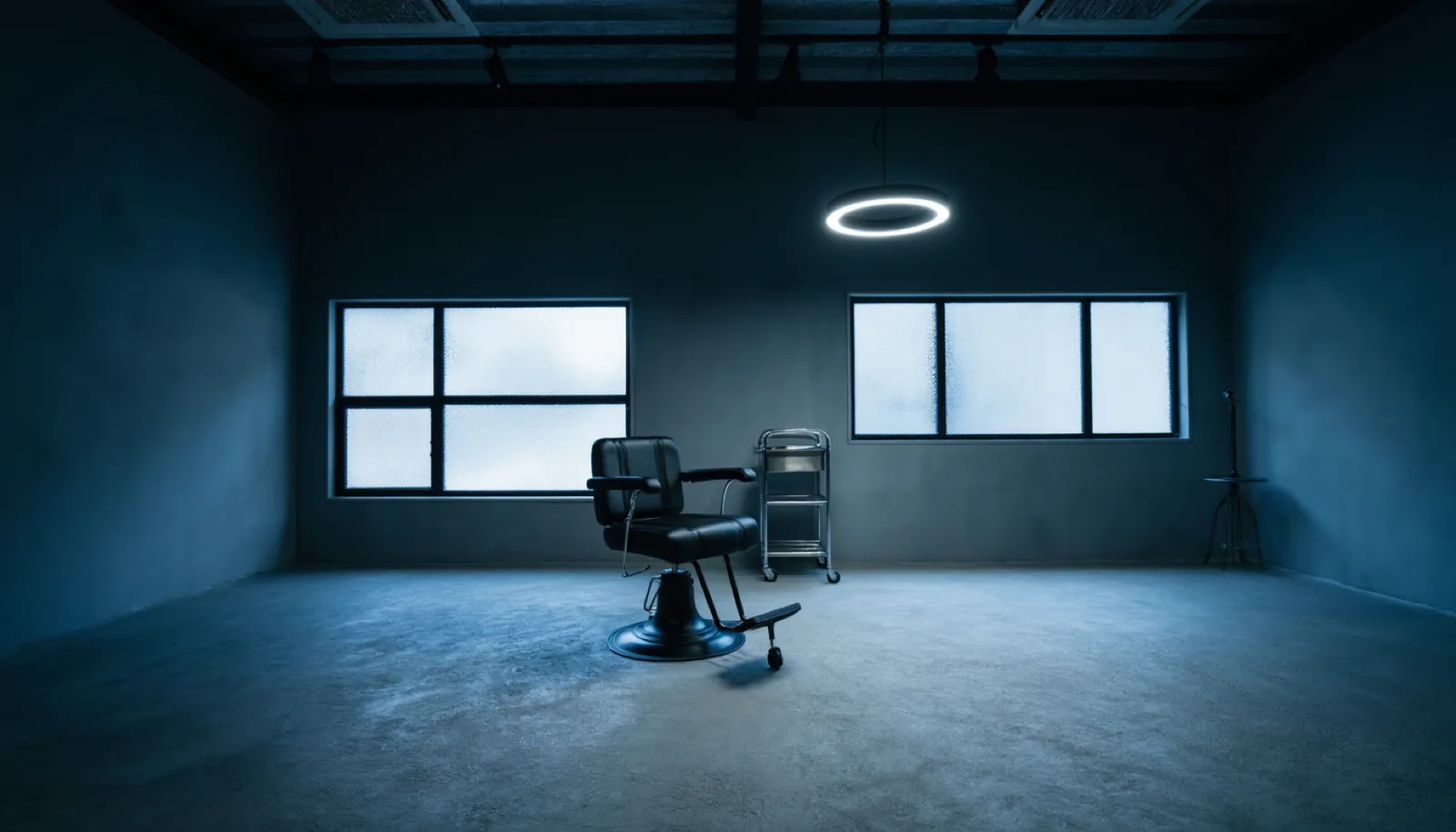 The empty studio: concrete floor, black steel factory windows and a single matte black barber chair under a ring light